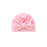The Pret my baby cotton woven turban cap for babies comes in light pink and features a large matching bow on the front, shown against a plain white background.