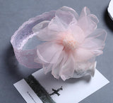 The Pret my baby Lace headband with large organza flower rests on a gray surface atop a black-and-white photo, making it the perfect elegant accessory for any outfit.
