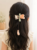 pretmybaby hairclip featuring a pastel organza tulip flower on a bow with a dangling bud worn in dark wavy hair