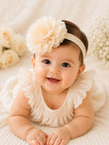 pretmybaby baby headband with a large pastel fluffy flower, worn by a smiling infant on a soft cream background.