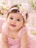 pretmybaby pastel baby headband with a layered rose, butterfly, and feathers worn by a smiling infant in a pink dress