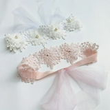 The Pret my baby lace headband features soft flower accents and pearls on delicate lace, beautifully displayed on a white surface—an elegant accessory for any outfit.