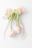 The Pret my baby "Tulip with pearls and delicate ribbon fascinator hairclip" features pastel pink and green ribbons, pearl accents, and tulip-shaped ornaments—perfect as a handcrafted baby hair accessory shown on a white background.