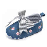 The Embroidery bellies with stripe bow - blue from Pret my baby features floral embroidery, a bold black-and-white striped bow, scalloped white edges, and a heel loop, making these baby shoes stylish and sweet.