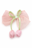 The Pret my baby Medium Fascinator Organza Tulip Bow features a decorative pink organza bow with a translucent texture, tied with a green ribbon and two small pink fabric flower buds, set against a white background.