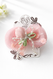 The Pret my baby Tulle curve bow with tulip and pearl ingrain fascinator hairclip features a pink satin design with sheer fabric, mini flowers, green ribbon, and pearl-like beads—an ideal handcrafted accessory for floral hair clip lovers.