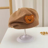 The Pret my baby Soft Woollen Knitted Beret Cap features a charming teddy bear design, ideal for babies or toddlers. Shown on a white stand with a neutral background.