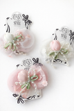 Three handcrafted Tulle Curve Bow with Tulip and Pearl Ingrain Fascinator hairclips by Pret my baby, featuring pastel pink and white fabric flowers, pearl beads, and green leaves, displayed on white background. Packaging shows the brand name.
