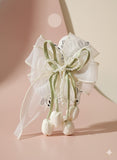 The Pret my baby Tulip with pearls large bow fascinator hairclip features sheer white ribbon, green accents, pearl strands, and satin tulip buds for a handcrafted look against a pink and cream background.