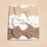 Pret my baby’s Pack of 3 headbands with large knot bows – style 7 features beige, white with a subtle print, and light brown stretchable bands, displayed vertically on a white card against a beige background.