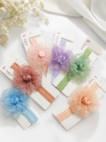 Six Pret my baby Fascinator large flower with bud baby headbands in pink, peach, purple, green, blue, and beige are arranged on white cards among delicate flowers and smooth draped fabric for a dreamy look.
