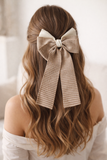 A woman with wavy, light brown hair styled half-up wears the pretmebabe Checkered Bow with trail Hair Clip in beige and white, its long tails adding classic glamour to her look, paired with an off-shoulder white top.