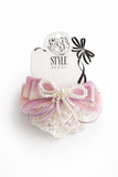 The Multiple bow with doiley lace fascinator hairclip by Pret my baby features pink and lavender ribbons, doiley lace, a pearl bow, and is set on an alligator pin. It comes on a white Style Seoul backing card with a black bow illustration.
