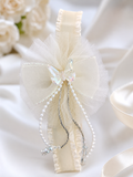 The Fancy fascinator crystal butterfly on bow baby headband by Pret my baby features an ivory satin band with a sheer tulle bow, crystal butterfly, silver and pearl accents—presented elegantly on white fabric with soft floral decor.