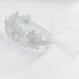 The Pret my baby Lace headband with soft flowers and pearls features delicate lace, floral accents, pearl-like beads, and a sheer white ribbon bow, shown on a white background. Ideal for complementing elegant outfits.