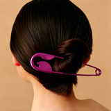 A woman with dark hair in a bun, secured by the Pretmebabe Safety Pin bun clip, is photographed from behind against a plain beige background.