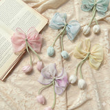 Five pastel Medium Fascinator Tulip Bows by Pret my baby in pink, blue, yellow, purple, and mint green, each with two soft tulip accents, are displayed on lace fabric beside an open book.