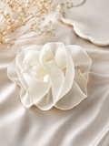 The Pret my baby Fascinator Pastel Chiffon Flower Hair Clip, a delicate handcrafted accessory with ribbon accents, rests on a silky surface beside dried baby's breath and a ceramic plate.