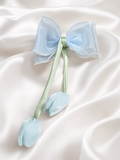 The Medium Fascinator Tulip Bow with Beads Lining by Pret My Baby features a delicate organza bow, beaded edges, two green ribbon tails with blue fabric buds, all set on smooth white satin.