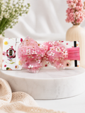 A Pret my baby soft cotton everyday baby headband with a tiny flowers tulle bow sits atop a decorative white floral box on a round marble surface, blurred blooms in the background.