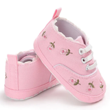 The Pret my baby Embroidery sneakers - pink feature delicate floral embroidery, white soles, and laces. One pre-walker shoe stands upright while the other leans against it, highlighting charming side and back details.